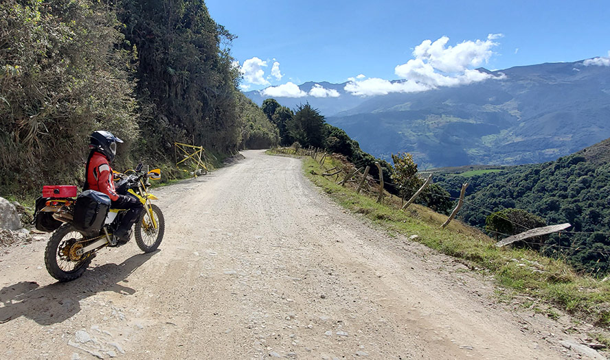 Dirt Bike and rider parked on gravel mountain road overlooking valley scene