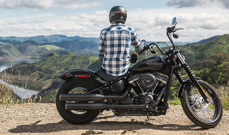 Parked up Harley-Davidson motorbike with rider sat on seat overlooking the valleys below and blue sky 