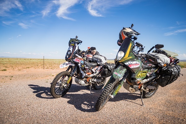 2 Amsoil dirt bikes parked by the side of a road 